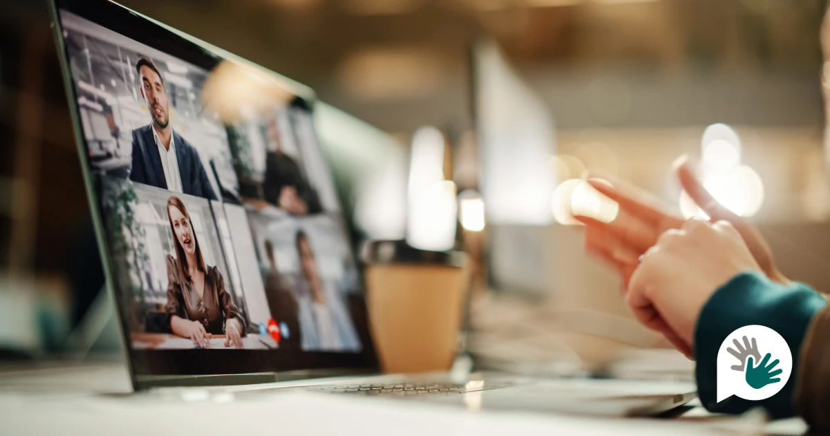 Person using British Sign Language during a video conference on a laptop, with multiple participants visible on screen, highlighting accessible remote meetings and inclusive online communication.